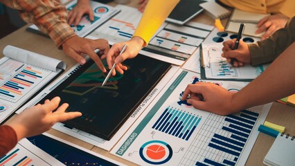 A dynamic office scene featuring hands collaborating over business reports, charts, and a tablet with data visualization tools, highlighting teamwork and strategic planning. SACTR