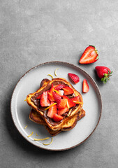 Toasted bread with chocolate cream and strawberries on a plate on a dark background with fresh berries.