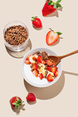Greek yogurt with chocolate granola, strawberries and banana in a bowl on a beige background