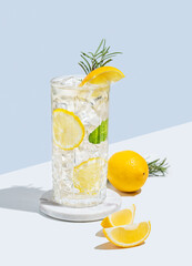 Lemonade with lemon, rosemary and ice in a glass on a white  blue background with shadow and fruits.