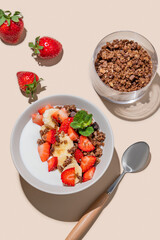Greek yogurt with chocolate granola, strawberries and banana in a bowl on a beige background