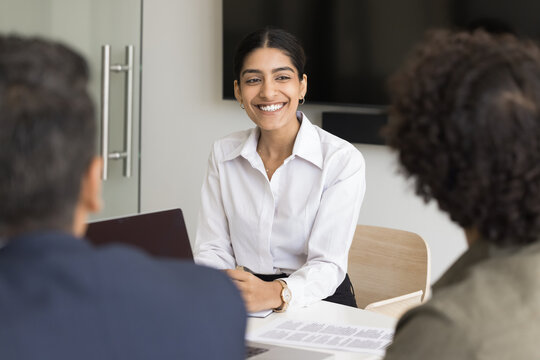 Attractive confident Indian woman take part in office meeting with colleagues or partners, smile, listen, enjoy communication, passing successfully job interview. Human resources, headhunting process