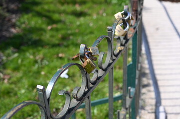 Metal fence with padlocks symbolizing love and commitment. Romantic tradition of couples leaving locks on a bridge or railing. Close-up detail in sunlight.