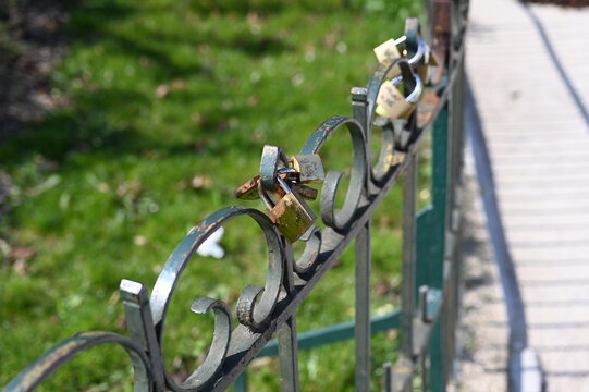 Metal fence with padlocks symbolizing love and commitment. Romantic tradition of couples leaving locks on a bridge or railing. Close-up detail in sunlight.