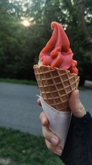 Cyclist holding red fruit strawberry ice cream in waffle cone during sunset