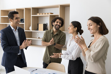 Group of four colleagues standing together in office, engaging in positive and celebratory moment,...