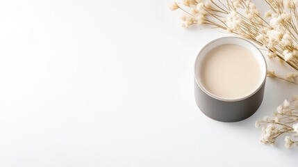 Creamy, light-beige drink in a dark gray bowl, beside dried white flowers
