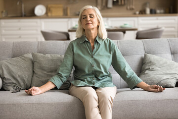 Mindfulness and meditation. Calm peaceful older female pensioner rest on couch at home practice...
