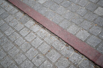 Fototapeta premium Stone pavement with red line marking. Urban cobblestone texture background, old European street detail.