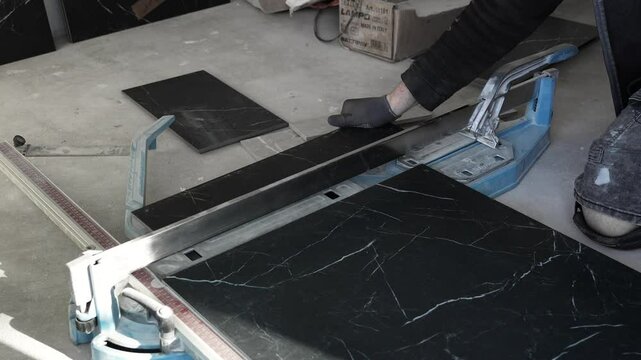 Master tiler cuts and breaks black porcelain tiles on a dry tile cutter