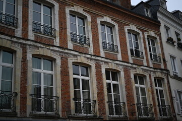 Naklejka premium classic French brick façade with tall white-framed windows and elegant wrought-iron balconies. Historic European architecture under an overcast sky, creating a timeless and authentic urban atmosphere.