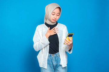 Young Asian woman in hijab looking at her smartphone with a touched and emotional expression,...