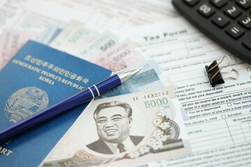 North Korean won money bills lies on table with pen, calculator, passport and tax forms