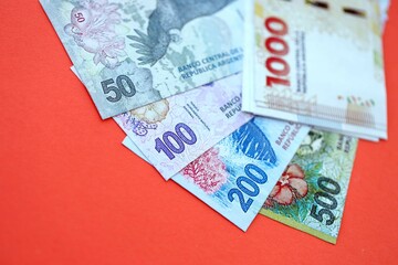 Argentine pesos money bills in big amount lies on red color table close up