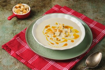 Cauliflower puree soup with white bread croutons and aromatic butter as a garnish in a light ceramic plate on a green concrete background. Recipes cauliflower. Healthy food