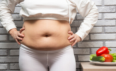 Close-up of the belly with fat. Women's health. A woman dressed in sports clothes shows off her...