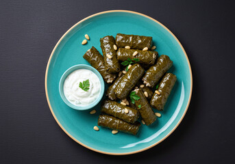 A high resolution photo of stuffed grape leaves with a side of tzatziki, arranged on a teal ceramic dish. Centered plating, bold contrast with the rich black background for visual impact.