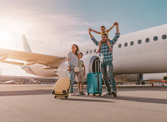 A happy family is at the busy airport, surrounded by luggage, eagerly preparing for their next...