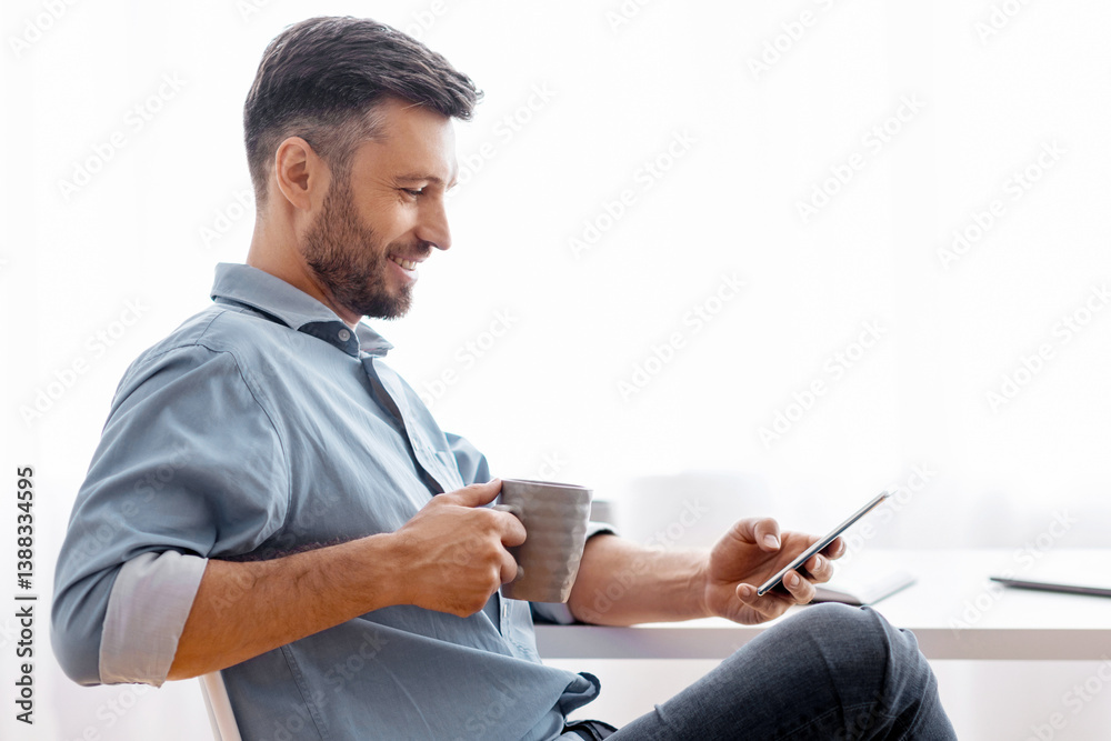 Poster break in work. relaxed male freelancer using smartphone and drinking coffee while sitting at desk at