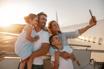 A joyful family takes a delightful selfie at the airport during a sunset, celebrating their...