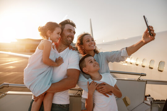 A joyful family takes a delightful selfie at the airport during a sunset, celebrating their exciting adventure