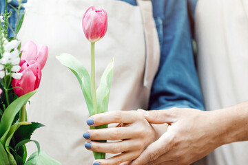 Couple of family small business owners make beautiful fresh bouquet for client. Young male florist teacher woman in apron to make composition with tulips at flower shop outdoor, cropped, vertical