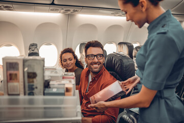 A friendly flight attendant joyfully engages with smiling passengers during inflight service and...