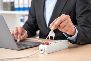 Close up of man hand plugging plug on a power strip socket using laptop on a desk at office