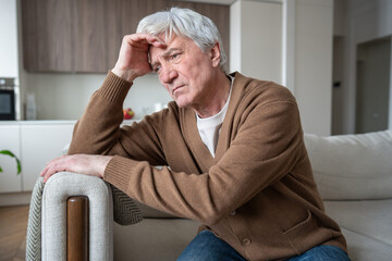 Frustrated sad old man with Alzheimer sitting abandoned on sofa at home with blank stare. Memory...