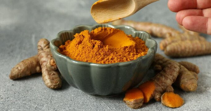 Woman taking tumeric powder with spoon at grey table, closeup
