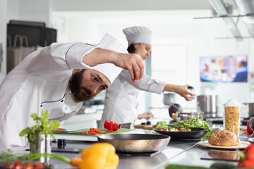 Dedicated male chef garnishing a dish with freshly cut vegetables on the stove, ensuring each plate...