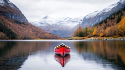 Tranquil red canoe on a serene alpine lake, surrounded by autumn foliage and snow-capped mountains