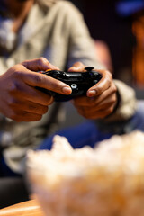 Focused young adult participates in online shooter video games at home, having fun with gaming tournament while he has popcorn snack in the living room. Smart tv modern setup.