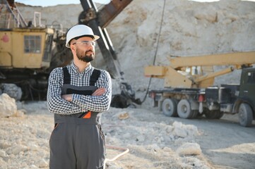 A worker in a helmet stands on the background of an excavator in a quarry