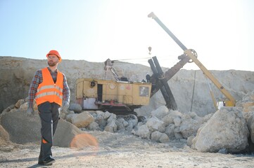 A worker in a helmet stands on the background of an excavator in a quarry