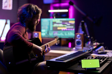 Young singer playing guitar and practicing with online tutorial lessons, looks at daw software on...