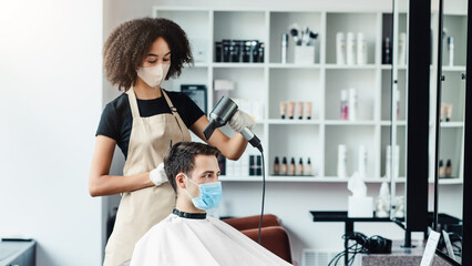 Hairdresser drying hair of male client, both observing safety measures, empty space