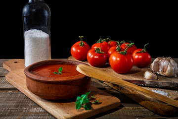 A bowl of tomato sauce and ingredients to prepare it in a rustic context.