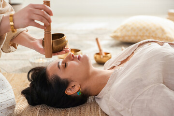 Fototapeta na wymiar Woman undergoing singing bowl therapy lying on floor indoors