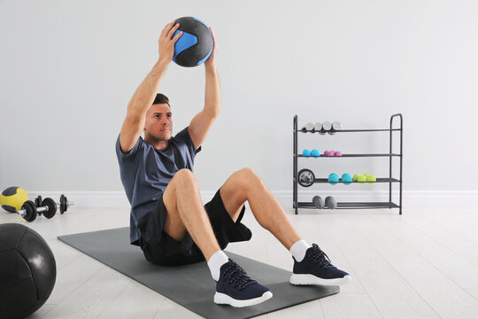 Muscular man doing sit ups with medicine ball on mat in modern gym - Powered by Adobe