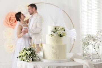 Happy married couple together indoors, focus on wedding cake and bouquet on table