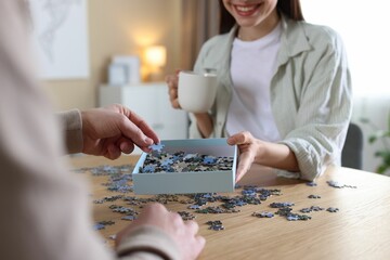Couple with puzzle pieces at wooden table indoors, closeup