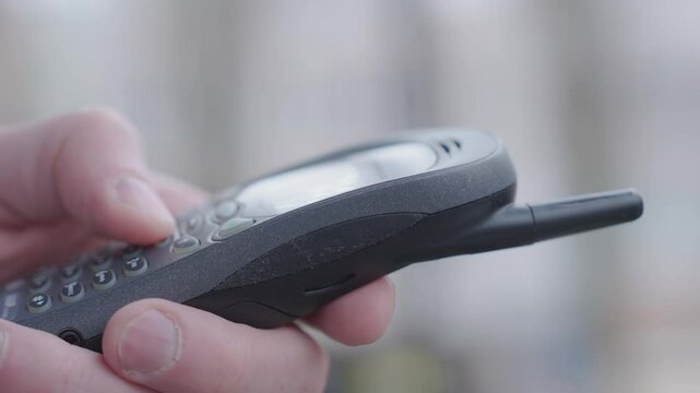 Hand Holding Old Mobile Phone with Buttons and Antenna Close-Up, Fingers Pressing Keypad on Vintage Cell Phone