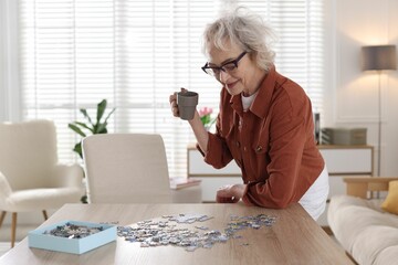Woman with cup of drink solving jigsaw puzzle at wooden table indoors