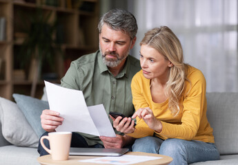 Married Middle Aged Couple Planning Budget Together, Reading Papers And Calculating Spends While...