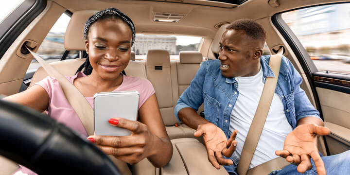 Watch the road. Emotional black man shouting at his wife checking smartphone while driving car, closeup. Indignant afro american guy sitting by female driver using smartphone, dont look at road