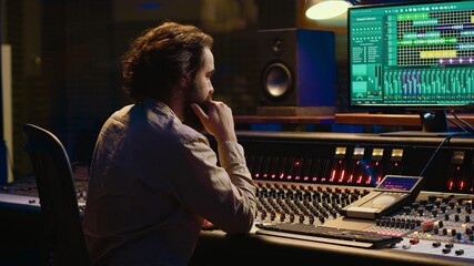 Music producer editing sounds with mixing console and switchers to remove tonal imbalances or white...