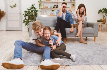 Exhausted Parents Covering Ears Looking At Naughty Children Playing Loudly At Home. Family Problems...
