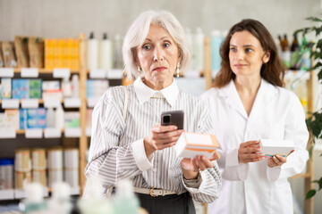 Senior woman in pharmacy scans QR code on omega 3 supplement. Health care, healthy lifestyle, prevention. Customer consulting with woman pharmacist about safe using pills.