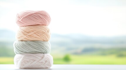 Four balls of yarn are stacked, showcasing soft pastel colors pink, peach, mint, and white. The composition is simple, with a blurred outdoor background. The image is high-quality, with soft lightin
